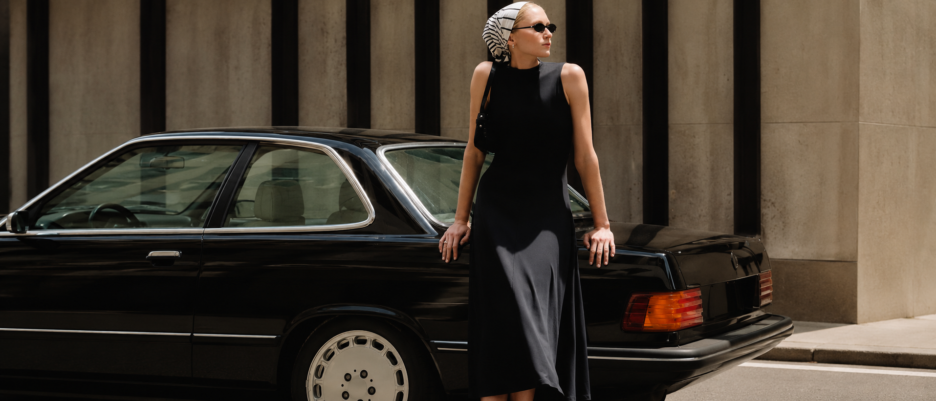 Woman wearing a refined black dress beside a classic car